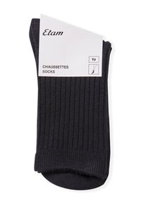 Calcetines negros acanalados, fabricados con material suave y con un diseño bajo. El embalaje incluye una etiqueta blanca con la marca e instrucciones de cuidado.