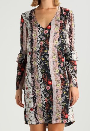 Kvinde iført en langærmet, V-hals blomstret kjole med lodrette striber i sort, pink, hvid og røde toner, med flæsedetaljer på ærmerne.