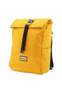 Mochila amarilla con diseño de parte superior enrollable, correas ajustables negras, hebilla azul y un parche con el logo en la parte frontal. Presenta bolsillos laterales y tela texturizada.