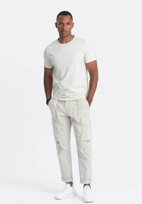 Camiseta gris claro de manga corta y cuello redondo, combinada con pantalones cargo beige claros con bolsillos laterales, llevados con zapatillas blancas.