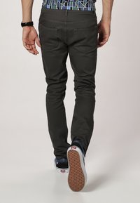 Slim-fit donkergrijze broek met achterzakken en zichtbare stiksels, gecombineerd met lage marineblauwe sneakers met een gestructureerde zool.