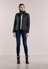 Black, quilted puffer jacket with a high collar and zip closure. Paired with fitted blue jeans and black ankle boots. Smooth texture.