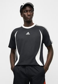 Svart sport-t-shirt med vita sidopanelaccenter, med rund hals och Adidas-logotyp på bröstet, kombinerad med mörka shorts.