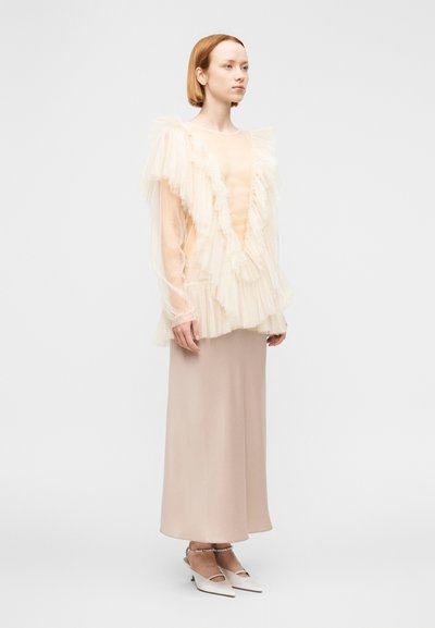 Αέρινο κρεμ τοπ με βολάν από τούλι, σε συνδυασμό με ανοιχτό μπεζ σατέν φούστα και λευκά παπούτσια με τακούνι. Λεπτές υφές, κομψός σχεδιασμός.