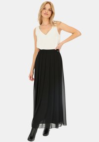 Czarna, plisowana długa spódnica z wysokim stanem, zestawiona z białą bezrękawnikową bluzką w serek, na neutralnym tle. Gładka faktura.