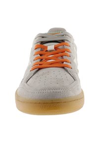 Sneaker grigia in suede con una suola in gomma texturizzata color beige, lacci arancioni e dettagli perforati sulla punta. Presenta accenti di branding bianchi.