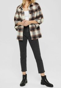 Rutig oversizejacka i krämfärgad och brun, med mörka knappar och två bröstfickor, i kombination med svarta skinny jeans och ankelskor.