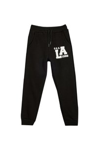 Pantalones de chándal negros con cintura elástica y cordón. Presenta bolsillos laterales y una impresión gráfica blanca que dice "U.S.A. LA 1986". Textura suave.