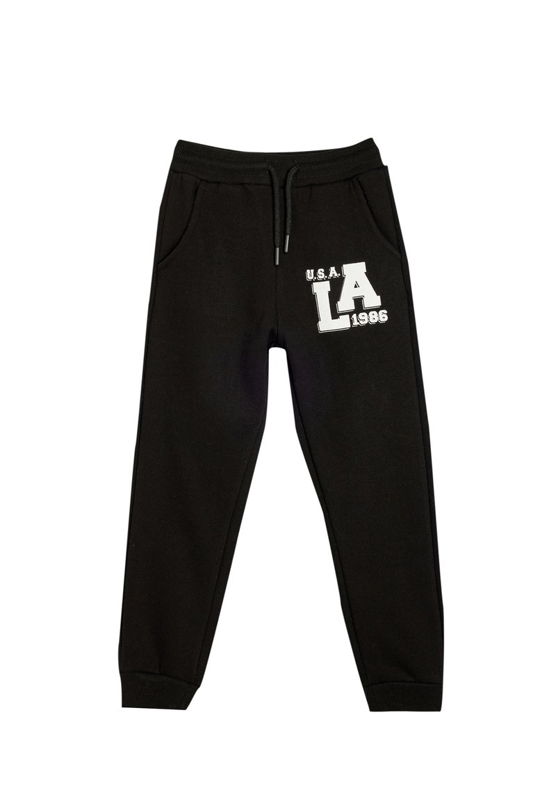 Pantalones de chándal negros con cintura elástica y cordón. Presenta bolsillos laterales y una impresión gráfica blanca que dice "U.S.A. LA 1986". Textura suave.
