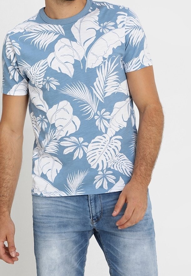 Homme portant un t-shirt à manches courtes avec imprimé feuilles tropicales bleu clair et un jean bleu délavé, debout les bras détendus.