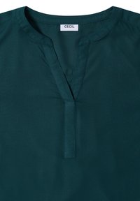 Blouse teal avec un décolleté en V et des manches courtes. Tissu lisse avec un léger éclat, présentant une petite fente et des détails de couture à l'avant.