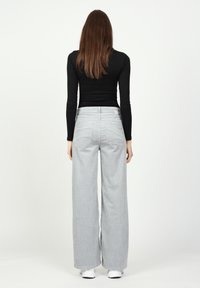 Graue weit geschnittene Hose mit Streifenmuster, ausgestattet mit hoher Taille, Gesäßtaschen und einem leicht ausgefransten Saum. Hergestellt aus einem strukturierten Stoff.