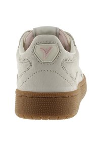 Zapatilla de ante blanca con un acento rosa en el talón, suela de goma texturizada y un logo hexagonal en la parte posterior, que presenta un detallado de costura.