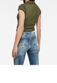 Olivgrön polo t-shirt med uppvikta ärmar, i par med ljusblå högmidjade jeans som har blekningar och bakfickor.