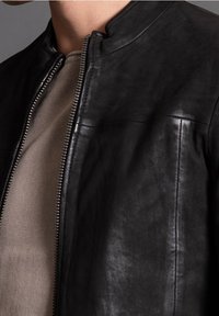 Svart läderjacka med slät textur, utrustad med ståkrage, dragkedja framtill och minimalistiska designelement.