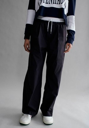 Schwarze leichte Hose mit einem elastischen Bund und einem Kordelzug. Sie haben eine lockere Passform und werden mit weißen Sneakern kombiniert.