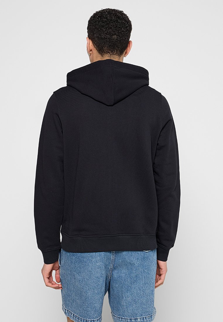 Felpa nera con cappuccio e finitura texturizzata. Presenta una tasca a marsupio e polsini a costine, abbinata a pantaloni shorts in denim chiaro.