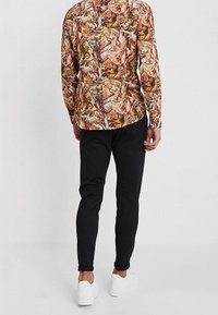 Langarmshirt mit einem mehrfarbigen künstlerischen Muster, kombiniert mit schwarzen Slim-Fit-Hosen und weißen Sneakers. Der Stoff wirkt glatt.