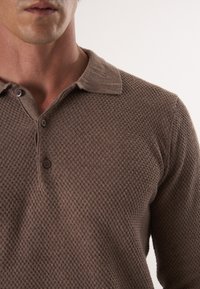 Bruine, gestructureerde poloshirt met een kraag en twee knopen bij de hals, die een wafelbreipatroon toont.