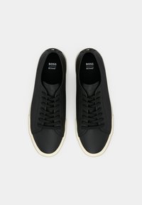 Black sneakers with a smooth, synthetic upper, featuring six eyelets and a cream rubber sole. Accented with logo printed on the insole.