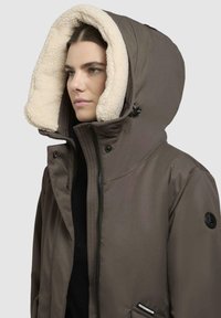 Brun isoleret jakke med en stor beige faux fur-forside kappe, lynlås lukning og frontlommer, der har et slankt, moderne design.