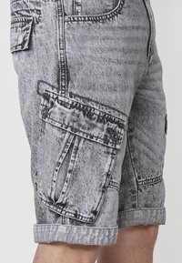 Shorts cargo dans un look en denim gris et noir délavé, avec de multiples poches, des ourlets roulés et une finition texturée.