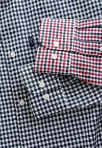 Camisas a cuadros con un patrón en azul marino y blanco, y un cuello a cuadros en rojo y blanco. Ambas tienen botones blancos y una textura de tela suave.