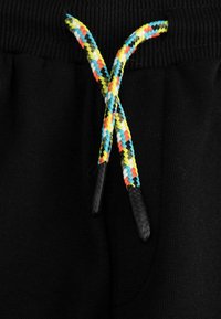 Czarne dresy z teksturowanym pasem, z multikolorowymi plecionymi sznurkami i czarnymi plastikowymi końcówkami.
