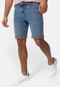 Shorts en denim bleu clair, avec une texture vieillie et des ourlets repliés. Associés à des baskets blanches avec un accent noir.