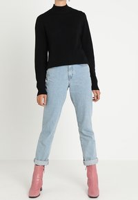 Zwarte gebreide trui met een hoge hals, gecombineerd met lichtblauwe opgerolde spijkerbroek en roze enkelboots.