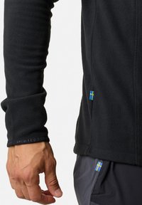 Schwarze Fleecejacke mit Reißverschluss vorne, ausgestattet mit einem eng anliegenden Bündchen und einem blau-gelben schwedischen Flaggenpatch nahe dem Saum.