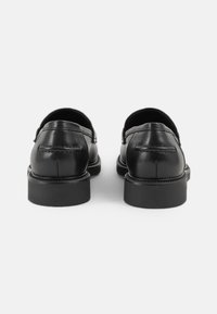 Pantofi din piele neagră cu o finisare netedă, cu vârfuri rotunjite și detalii minime de cusătură. Talpa groasă din cauciuc negru oferă stabilitate.