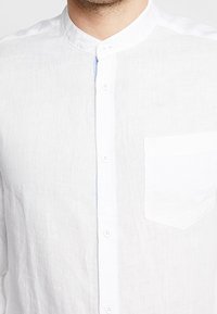 Biała lniana koszula z kołnierzykiem typu band, z przodu z guzikami i jedną kieszenią na piersi. Gładka faktura i lekki design.