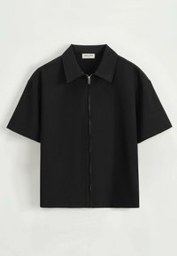 Chemise noire à manches courtes en tissu léger et lisse, avec une fermeture éclair à l'avant et un design de col classique.