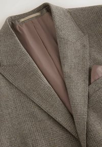 Grau-karierter Blazer mit glattem braunem Futter. Verfügt über spitze Revers und eine Brusttasche mit Taschentuch. Strukturiert.