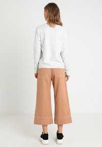 Maglione grigio a trama con scollo rotondo, abbinato a pantaloni beige a vita alta e gamba larga con cuciture a contrasto e sneaker nere.