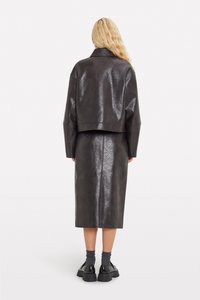 Black faux leather cropped jacket with wide sleeves, paired with a matching long skirt. Jacket has a smooth texture and minimal detailing.
