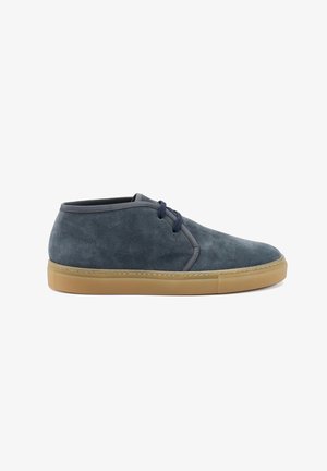Scarpe chukka in suede grigio con punta tonda, lacci blu e suola in gomma marrone chiaro, presentano un design minimalista e una texture morbida.