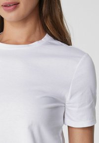 Weißes Baumwoll-T-Shirt mit Rundhalsausschnitt und kurzen Ärmeln, das eine glatte Textur und einen figurbetonten Schnitt aufweist.