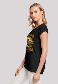 Camiseta negra con diseño gráfico amarillo que incluye el texto "Hakuna Matata" y una escena de El Rey León. De manga corta y corte relajado.