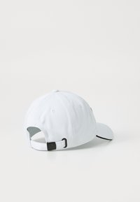 Hvit baseballcaps med buet brem, justerbar stropp bak og en tekstilstruktur. Har en liten logo på siden.