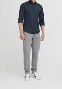 Marineblauw overhemd met lange mouwen en knopen, in een getailleerde pasvorm, gecombineerd met lichtgrijze spijkerbroek en witte sneakers met zwarte strepen.