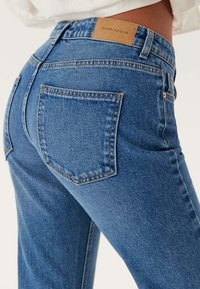 Högmidjade blåjeans med lätt stretch, med en beige läderetikett på baksidan och klassiska bakfickor. Slät denimtextur.