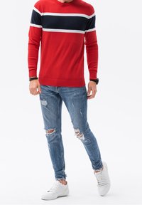 Rode trui met witte en marineblauwe strepen, gecombineerd met versleten blauwe jeans en witte sneakers. De trui heeft een ronde halslijn en geribbelde afwerking.