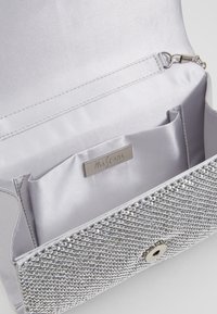 Pochette rigide argentée ornée de strass, intérieur en satin et emplacement pour cartes. Dispose d'une fermeture à pression et d'une étiquette de marque gravée.