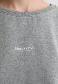 Sudadera gris hecha de una tela suave con un cuello acanalado. Presenta texto del logo en blanco "Marc O'Polo EST. EN ESTOCOLMO" en la parte frontal.