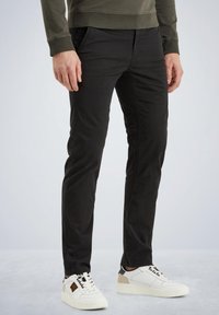 Črne bombažne hlače s slim fit krojem, ki imajo stranske žepke in gladko teksturo. Obute z belimi in bež supergami.