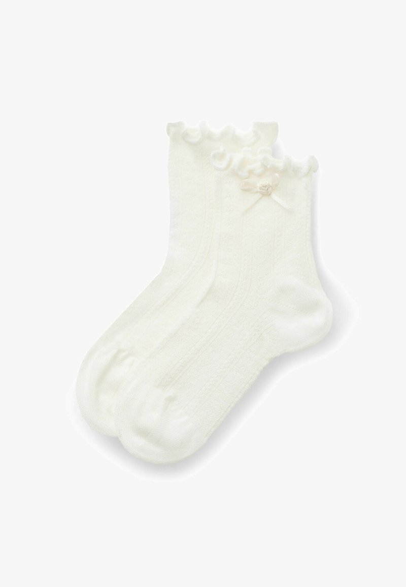 Chaussettes blanches à la cheville avec un bord supérieur volanté et un petit nœud décoratif sur chacune, tricotées avec un motif subtil.