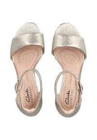 Bronzefarbene metallische Sandalen mit breiten Riemen, offener Zehenpartie und Knöchelverschluss. Glatte Textur, gepolsterte Innensohle und durchbrochene Details.