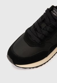 Mustad tennisjalats, mis on valmistatud sujuvatest ja tekstuursetest materjalidest, millel on pehmendustega keel, mustad paelad ja valge tallamärk.